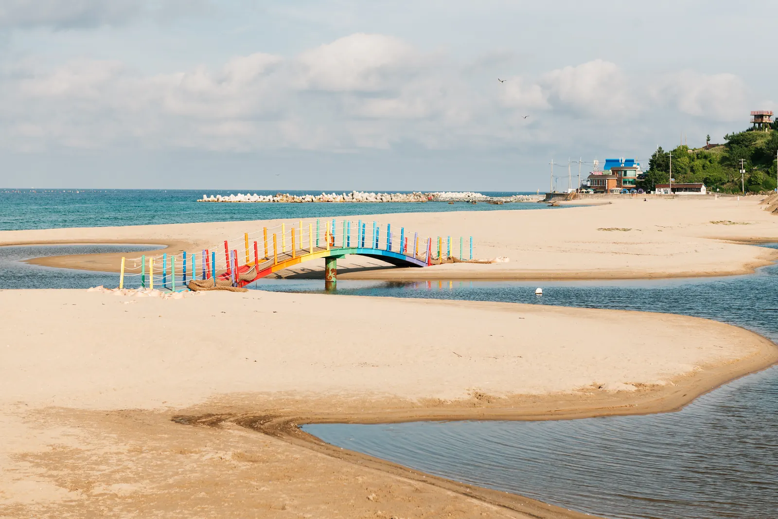 A sandbar reaching into the sea, with a rainbow footbridge